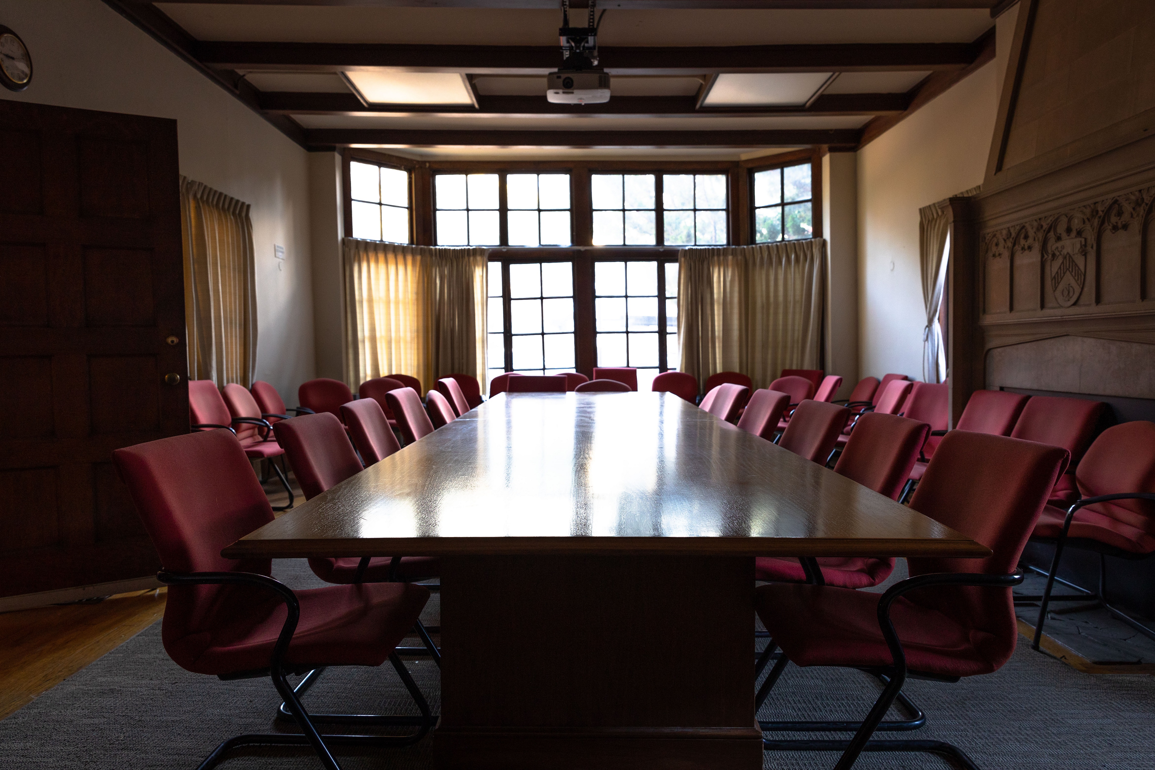 Long table surrounded by red chairs with tall windows in background.