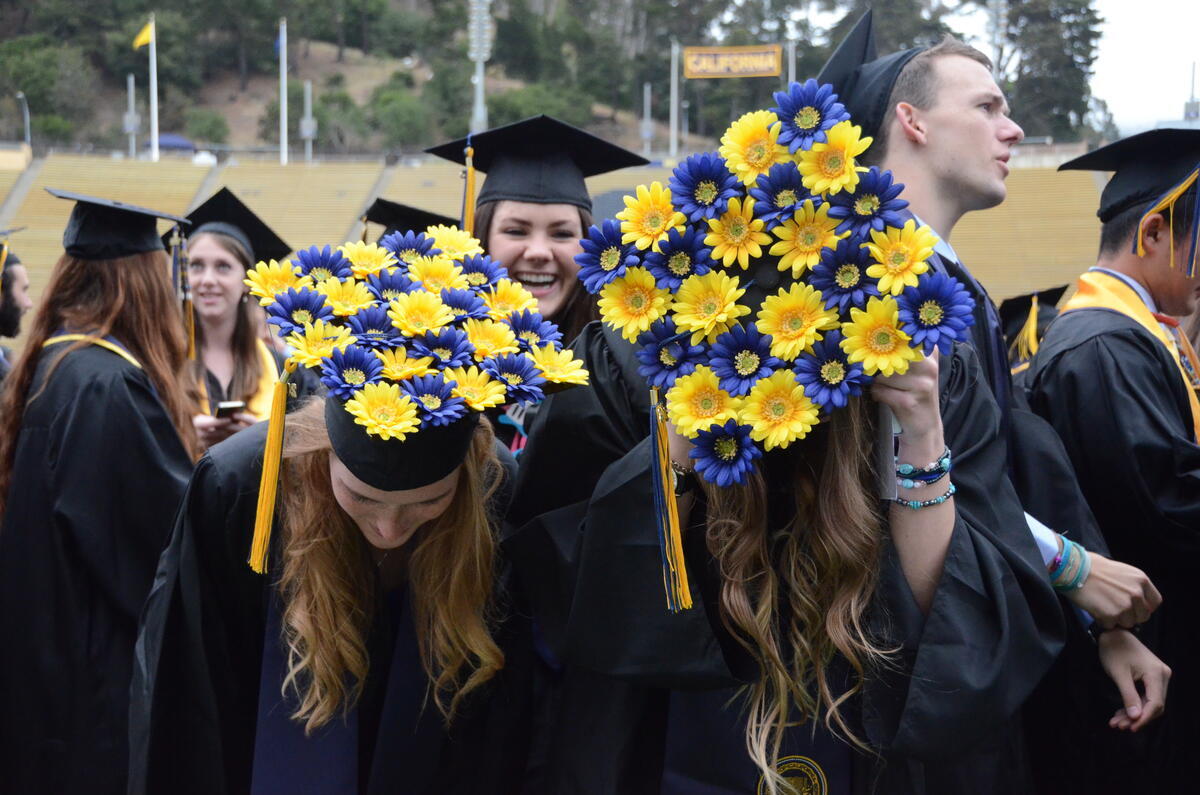 Two grads showing off their self-decorated caps covered with blue and yellow flowers.